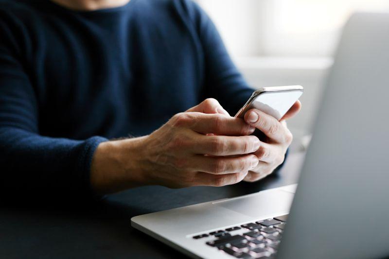 A person sitting behind their computer doing something on their phone