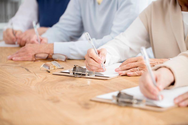 Three people sitting at a table filling in a questionnaire on paper.