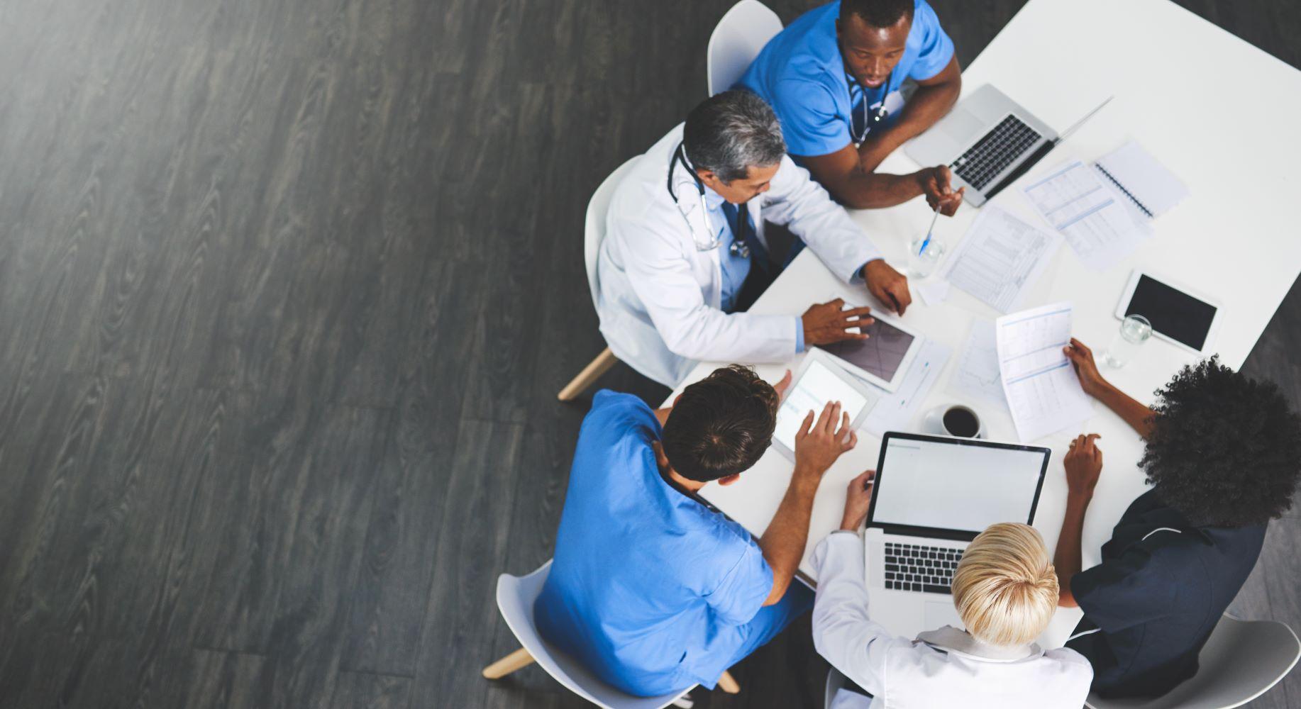 doctors and clinicians around a table with laptops having a meeting